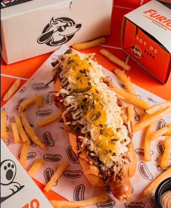 Perro caliente con pulled pork, queso y papa ripio sobre papel con perros dibujados