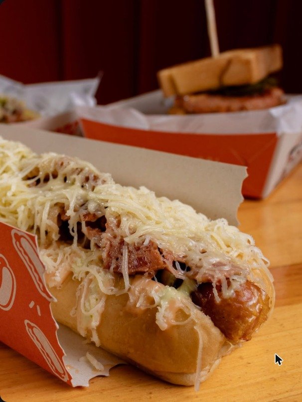 Perro caliente con pulled pork y queso gratinado en su empaque naranja